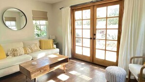 A living room with a wooden coffee table, a sofa with yellow cushions, a round mirror, and a sliding glass door with curtains. - Bright & Airy Culver City Home w/Garden Oasis. Walkable Location + WFH Ready! (Los Angeles)
