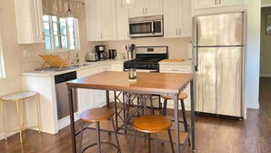 A kitchen with white cabinets, a wooden island with stools, a stainless steel refrigerator, and a microwave. - Bright & Airy Culver City Home w/Garden Oasis. Walkable Location + WFH Ready! (Los Angeles)