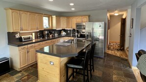 A modern kitchen with wooden cabinets, a central island with seating, stainless steel appliances, and a patterned floor. - Aspen Ridge-Mountain Adventure House in the Colorado Rockies-STR-0076-2026 (Fairplay)