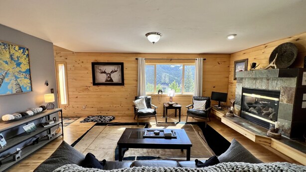 A cozy living room with a fireplace, wooden walls, a large window with a mountain view, a sofa, and a coffee table. - Aspen Ridge-Mountain Adventure House in the Colorado Rockies-STR-0076-2026 (Fairplay)