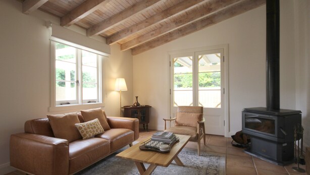 A cozy living room with a leather sofa, a wooden coffee table, a fireplace, and large windows allowing natural light. - Winton Cottage Maldon - Authentic Heritage Home. (Maldon)