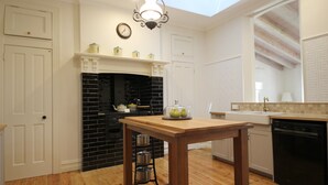A kitchen with a wooden table, a black tiled backsplash, a white door, and a clock on the wall. - Winton Cottage Maldon - Authentic Heritage Home. (Maldon)