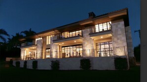 A modern two-story house with a balcony, large windows, and a well-lit exterior at dusk. - New Malibu Estate ~ Recording Studio, Tennis, Pool (Malibu)
