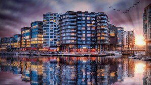 Hotel aan het water met meerdere balkons, een jachthaven en een zonsondergang op de achtergrond.