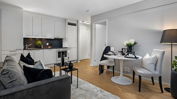 Een moderne keuken met witte kasten, een eethoek met een ronde tafel, en een bank met zwart-wit kussens.