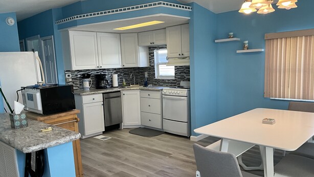A compact kitchen with white cabinets, a dining area with a table and chairs, and a small countertop with a microwave and other appliances. - Attention Snowbirds! (Fort Myers)