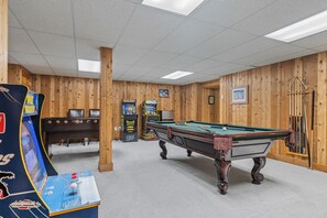 A pool table in a room with wooden walls, a pool table, and arcade games.