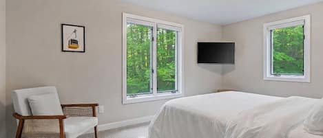 A bedroom with a bed, a chair, a television, and two windows.