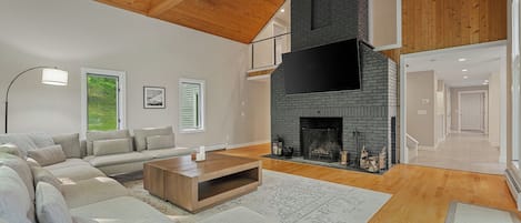 A spacious living room with a large sectional sofa, a fireplace, and a high ceiling with exposed wooden beams.