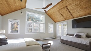 Une chambre avec deux lits, de grandes fenêtres, un ventilateur de plafond et un téléviseur fixé au mur.