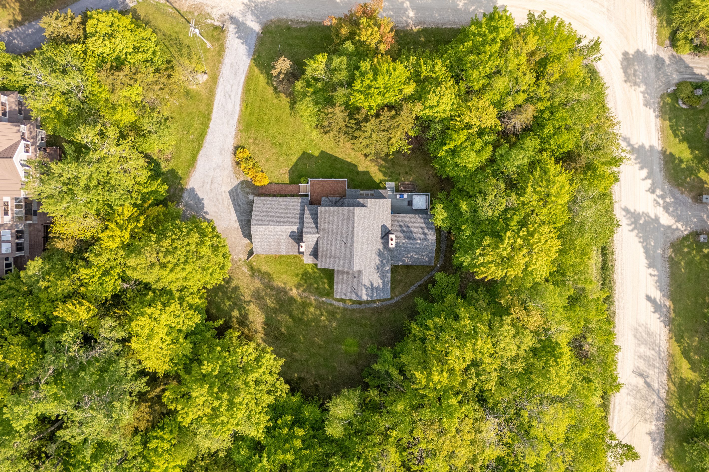 An aerial view of a residential property with a house, a driveway, and surrounding greenery.