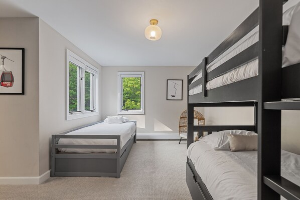 A bedroom with bunk beds, a window with a view of greenery, and a framed picture on the wall.