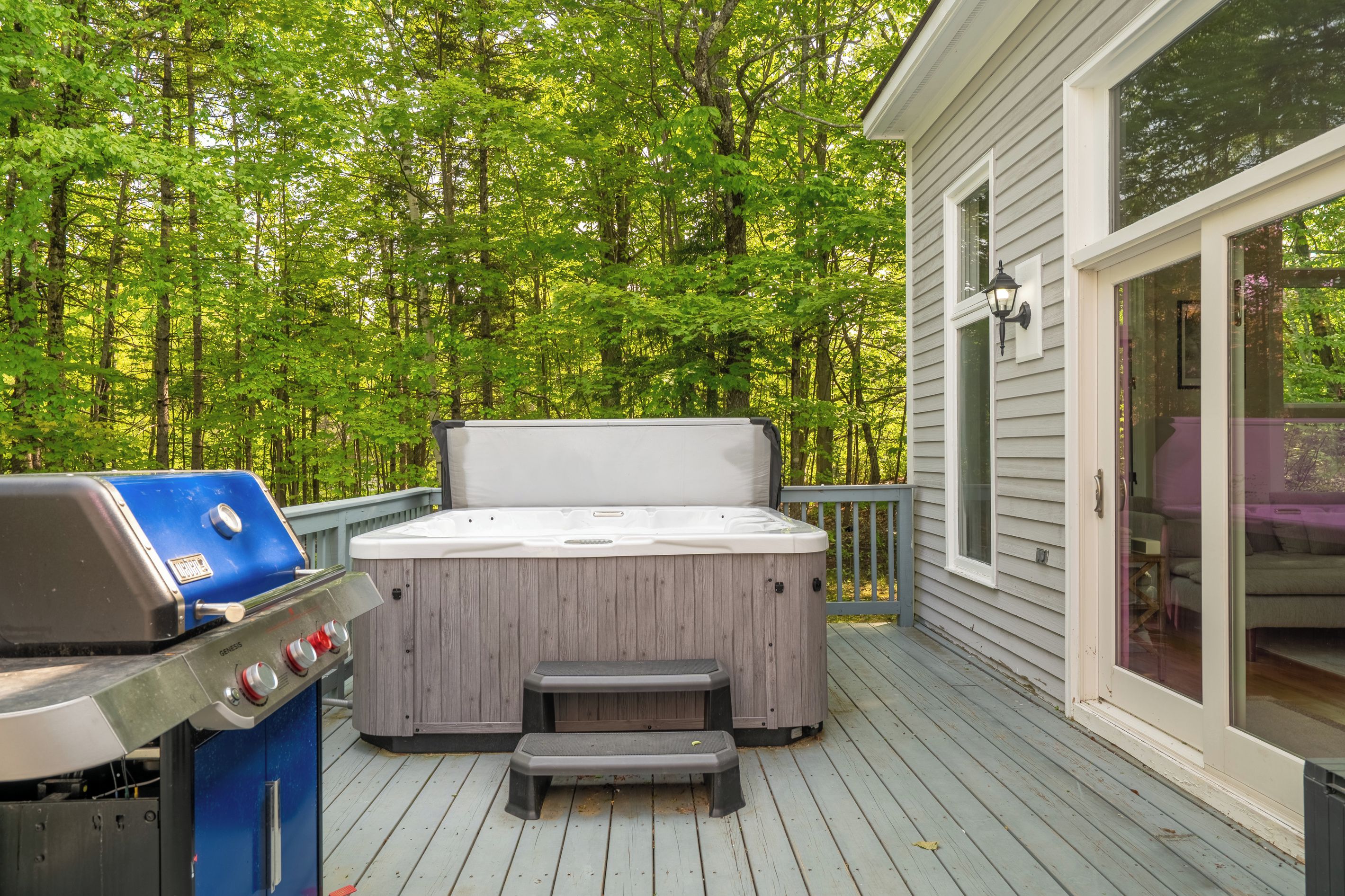 Une terrasse dotée d’un jacuzzi et d’un barbecue, entourée d’une forêt.