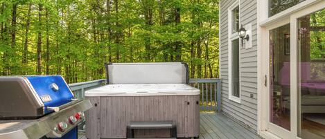 Une terrasse dotée d’un jacuzzi et d’un barbecue, entourée d’une forêt.