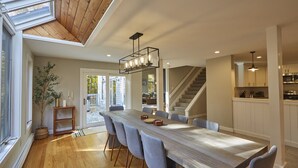 Un vaste espace dédié à la salle à manger, avec une longue table en bois, des chaises à revêtement gris et un luminaire suspendu au design moderne.