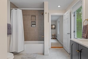 Un baño moderno con bañera, ducha y tocador con ventana.