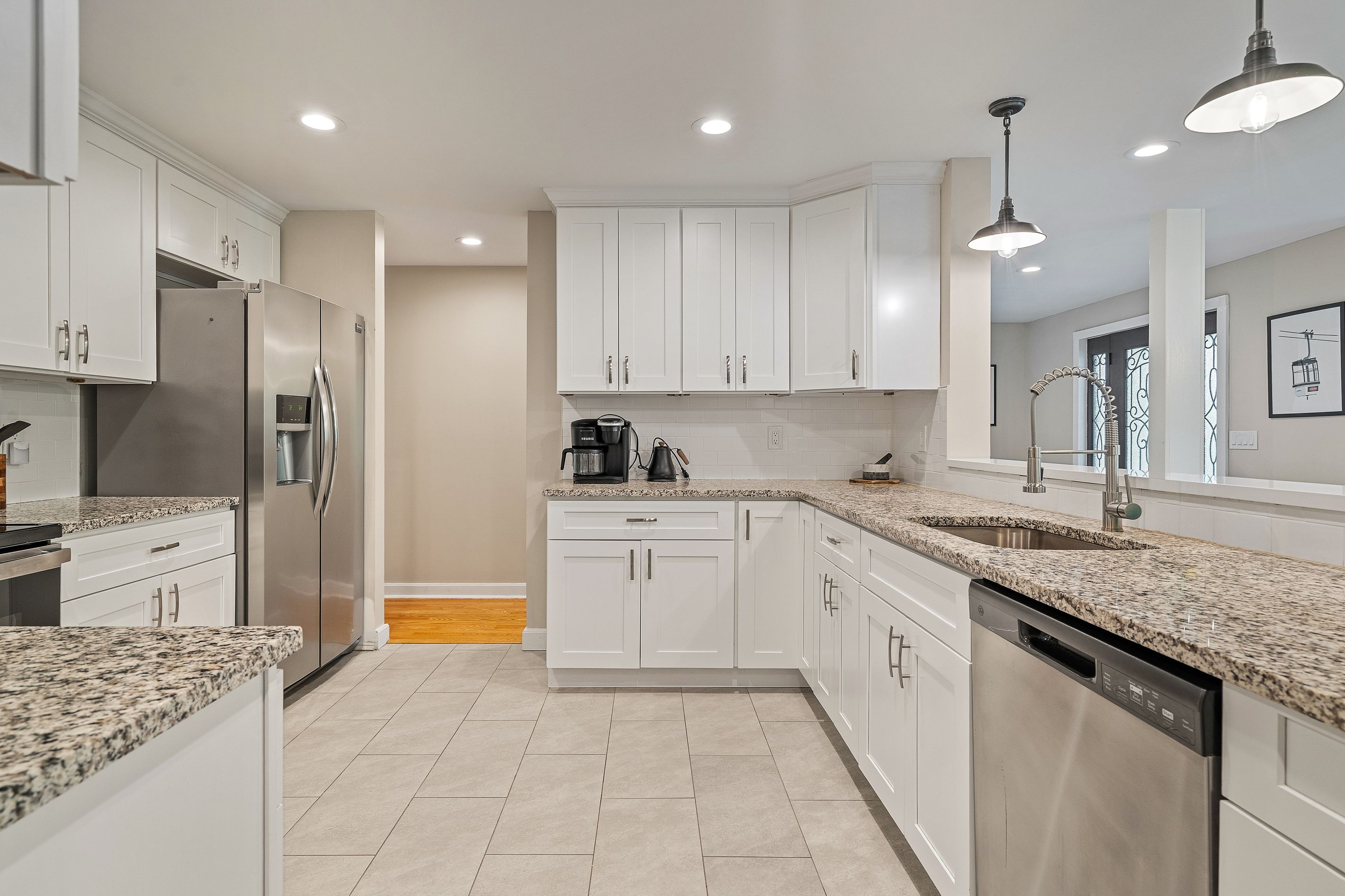 A modern kitchen with white cabinetry, granite countertops, stainless steel appliances, and recessed ceiling lighting.