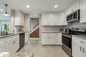 A modern kitchen with white cabinetry, granite countertops, a built-in oven, microwave, and a dishwasher.