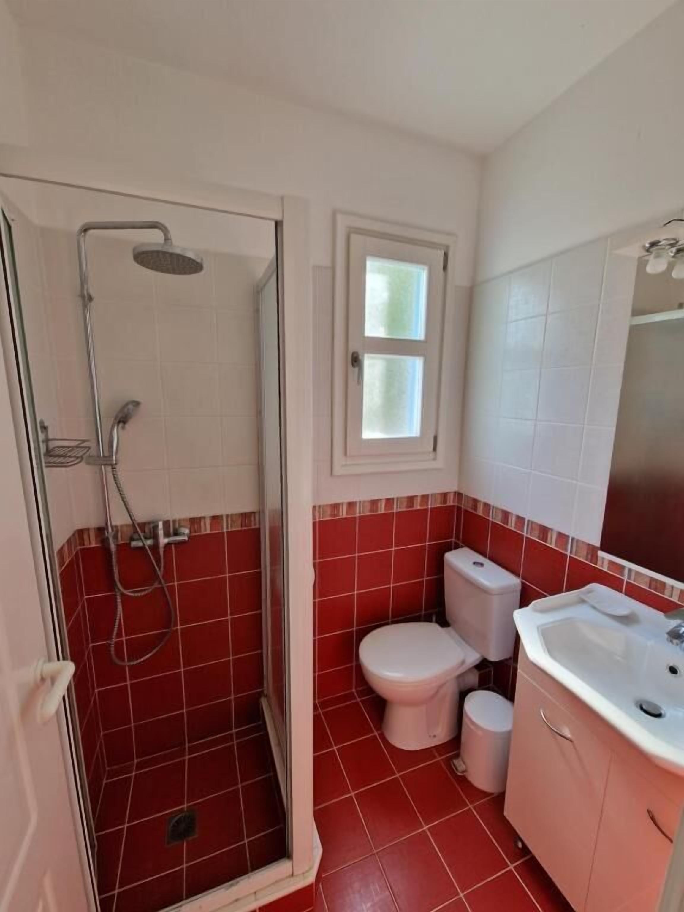 Un bagno con doccia, WC, lavandino e finestra.