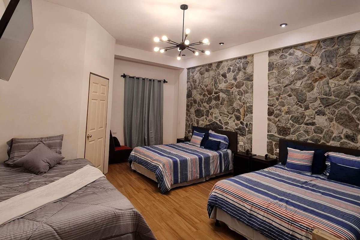 A bedroom with three beds, a stone wall, a wooden floor, and a ceiling fan.