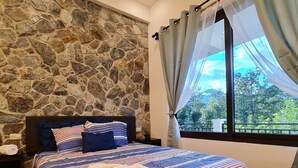 Une chambre avec un mur en pierre, un grand lit avec une literie à rayures, une table de chevet et une fenêtre avec des rideaux.