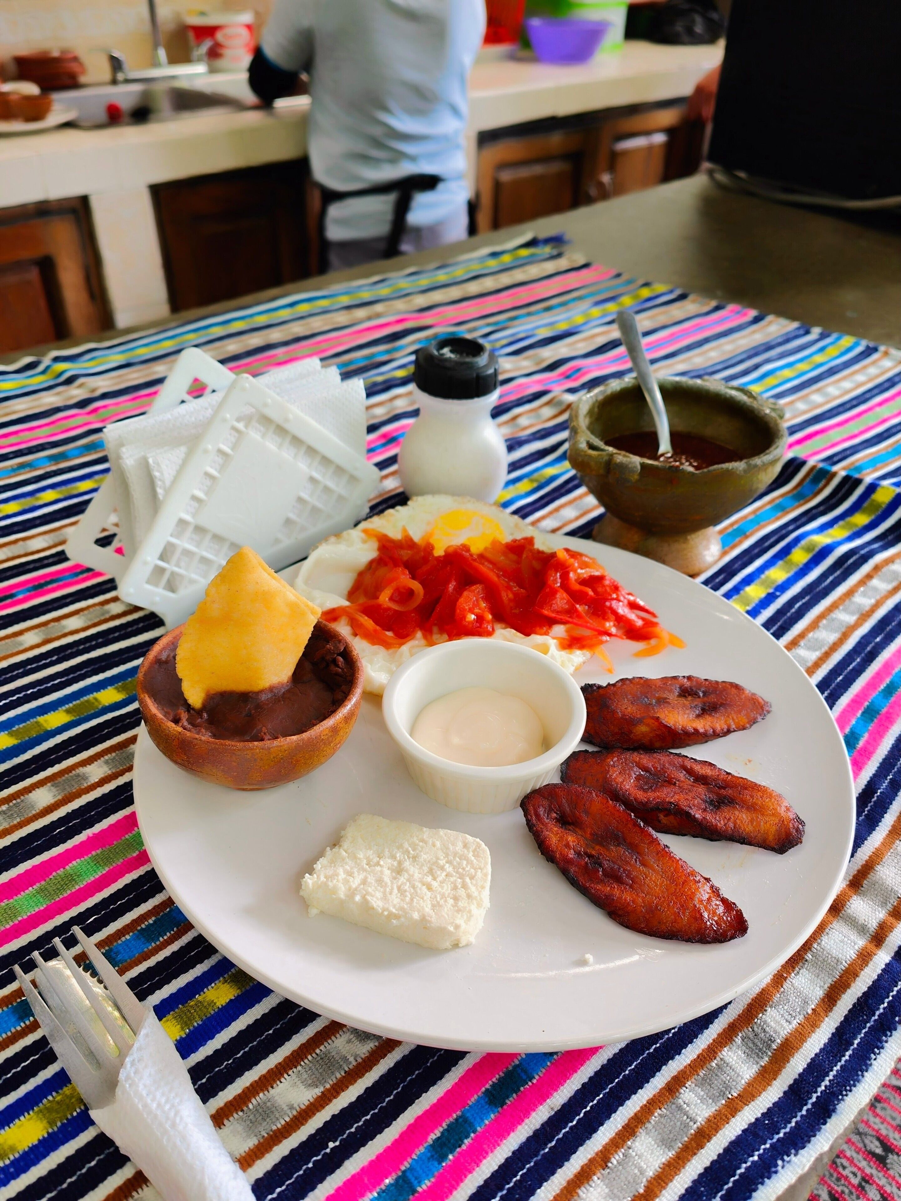 Un piatto di cibo con diversi elementi, tra cui platani fritti, una ciotola di fagioli e una piccola porzione di salsa.