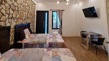 A bedroom with a stone wall, a bed with a floral quilt, a TV, and a desk with chairs.