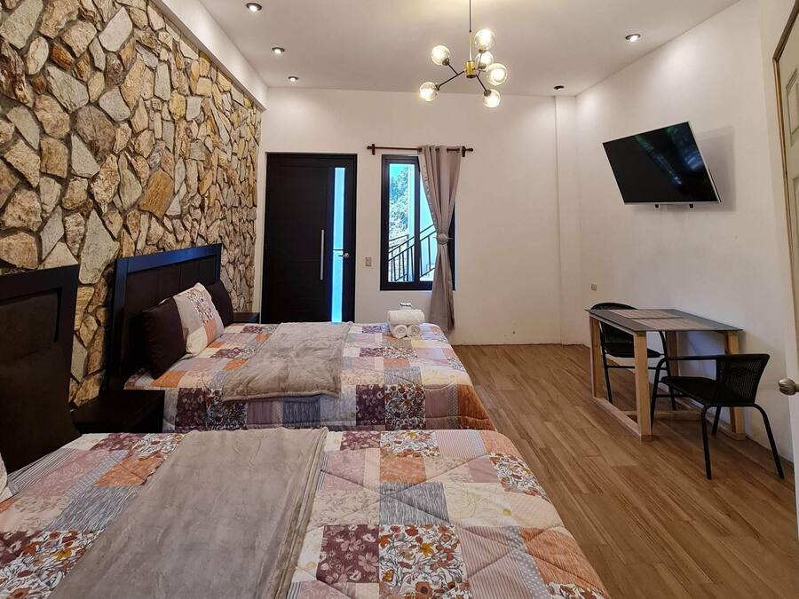 A bedroom with a stone wall, a bed with a floral quilt, a TV, and a desk with chairs.