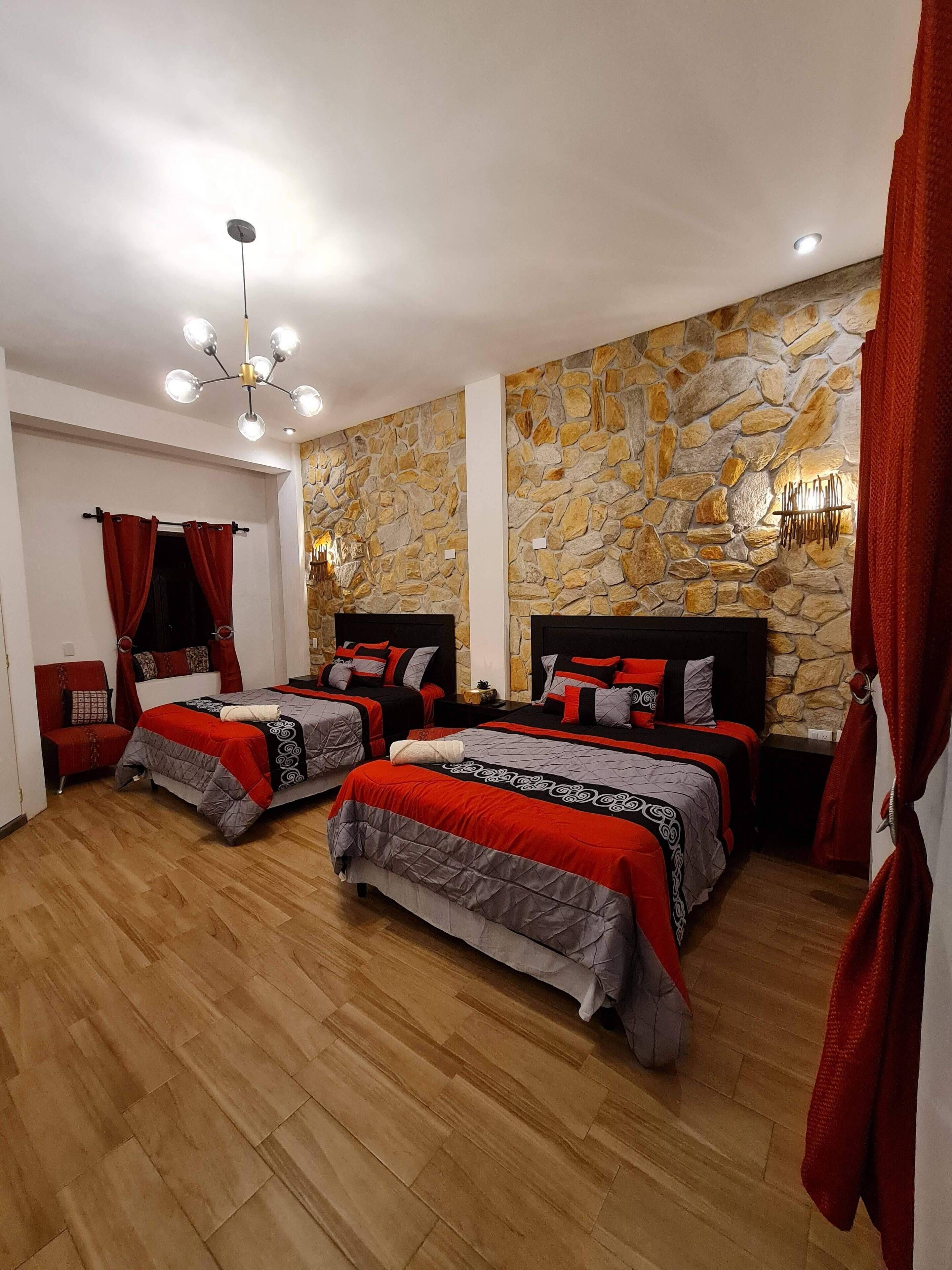 Un dormitorio con dos camas, paredes de piedra, suelo de madera y cortinas rojas.
