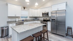 A modern kitchen with white cabinets, stainless steel appliances, granite countertops, and a central island with stools.