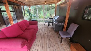 Un espace extérieur abrité comprenant un canapé rouge, une table, des chaises et un barbecue.
