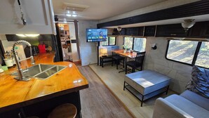 A compact kitchen with a wooden countertop and a built-in sink, a dining area with a bench and table, and a TV mounted on the wall. - Forest Cabin - Hot Tub - Fast WiFi - Fire Pit On Site (Duncan)