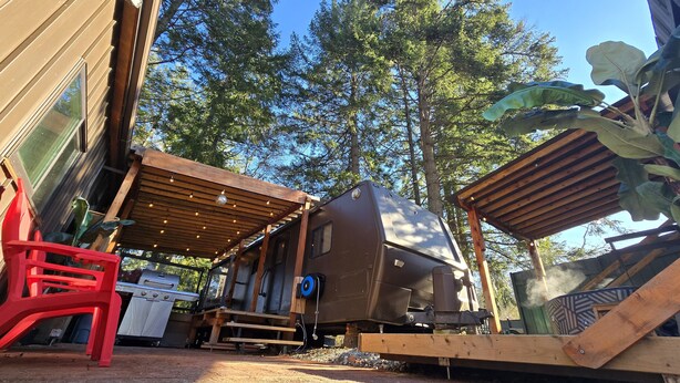 A recreational vehicle (RV) parked under a wooden pergola with a grill and a red plastic chair nearby. - Forest Cabin - Hot Tub - Fast WiFi - Fire Pit On Site (Duncan)