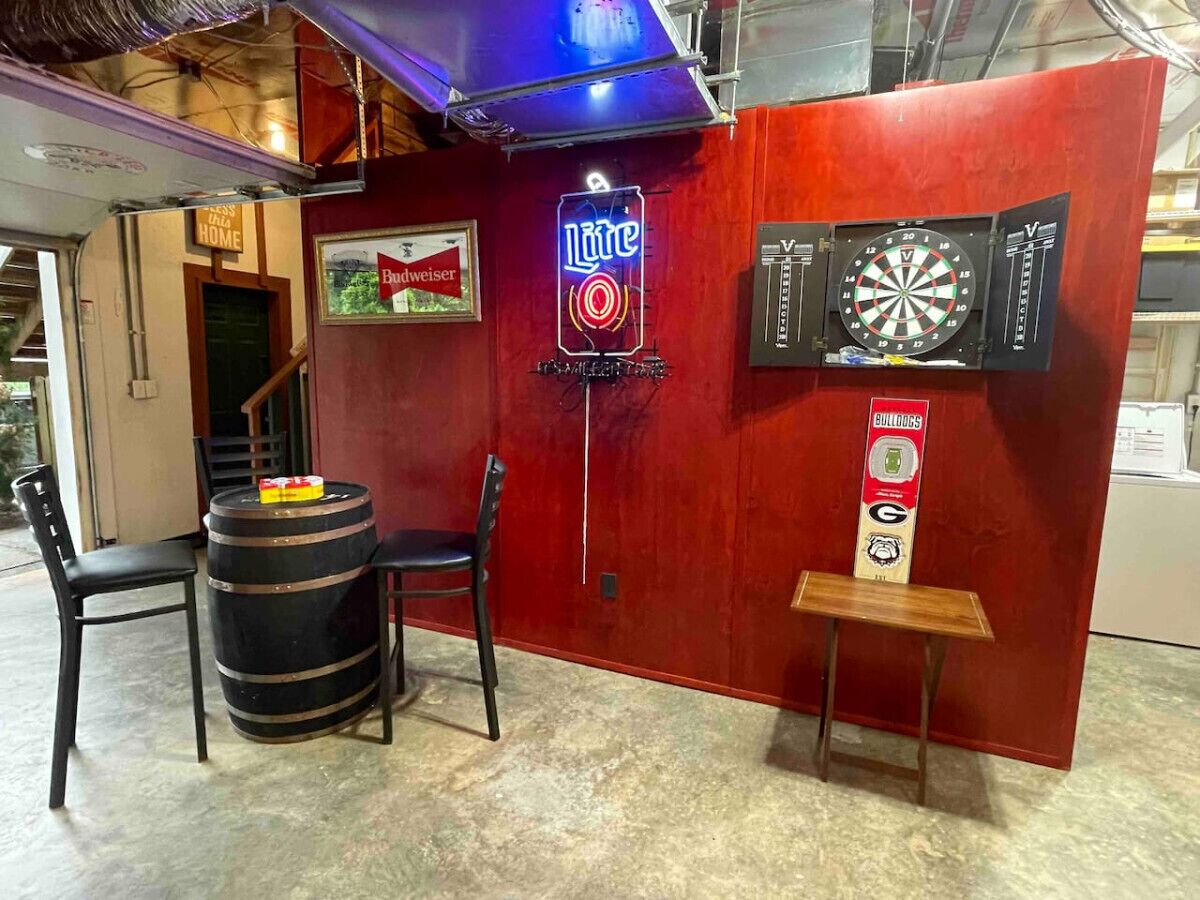 A bar area with a neon sign, dartboard, and stools.