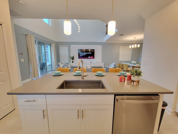 A modern kitchen with a central island, stainless steel appliances, and a dining area with yellow chairs.