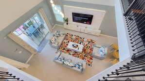 A spacious living area with a large flat-screen TV mounted on the wall, a sofa set, a coffee table, and a patterned rug. - Disney World/Private Swimming Pool, 5bed/5bath 5mins away to Oasis Club
 (Davenport)