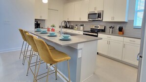 A modern kitchen with white cabinets, a central island with bar stools, stainless steel appliances, and pendant lighting. - Disney World/Private Swimming Pool, 5bed/5bath 5mins away to Oasis Club
 (Davenport)