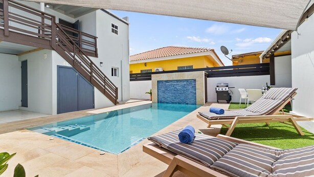 A modern outdoor pool area with lounge chairs and a staircase leading to an upper level. - BRAND NEW Central Modern Ground Studio with Pool (Noord)