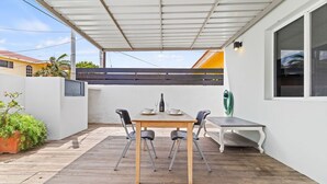 A covered patio with a wooden table and chairs, a small table, and a green hose. - BRAND NEW Central Modern Ground Studio with Pool (Noord)