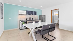 A modern kitchen with a dining area, featuring a white table, grey chairs, and a stainless steel stove. - BRAND NEW Central Modern Ground Studio with Pool (Noord)