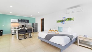A modern hotel room with a bed, bedside table, and a kitchenette area including a stove and microwave. - BRAND NEW Central Modern Ground Studio with Pool (Noord)