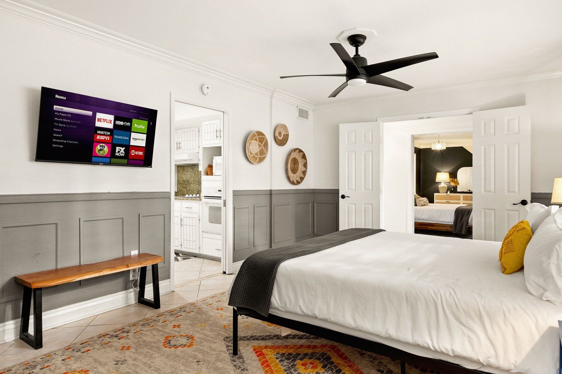 A bedroom with a bed, a bench, a ceiling fan, and a TV displaying streaming services.