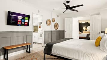 A bedroom with a bed, a bench, a ceiling fan, and a TV displaying streaming services.