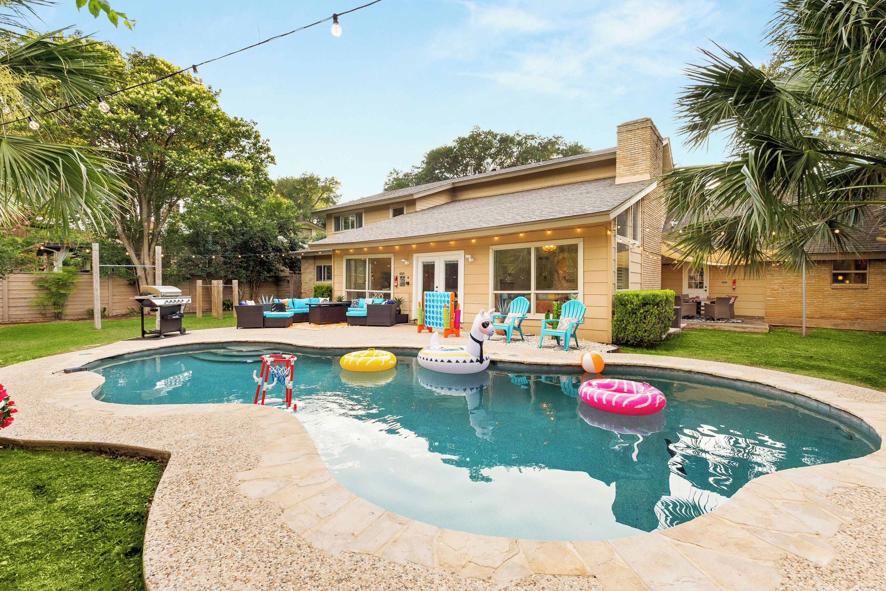 A residential backyard with a swimming pool, outdoor furniture, and a covered patio area.