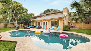 A residential backyard with a swimming pool, outdoor furniture, and a covered patio area.
