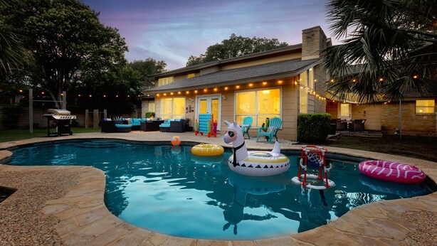 A backyard with a swimming pool, inflatable toys, and outdoor furniture. - 6BR Pool & Game Arcade | Family + Dog Friendly (San Antonio)