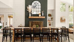 A dining area with a brick fireplace, wooden table, and black chairs. - 6BR Pool & Game Arcade | Family + Dog Friendly (San Antonio)