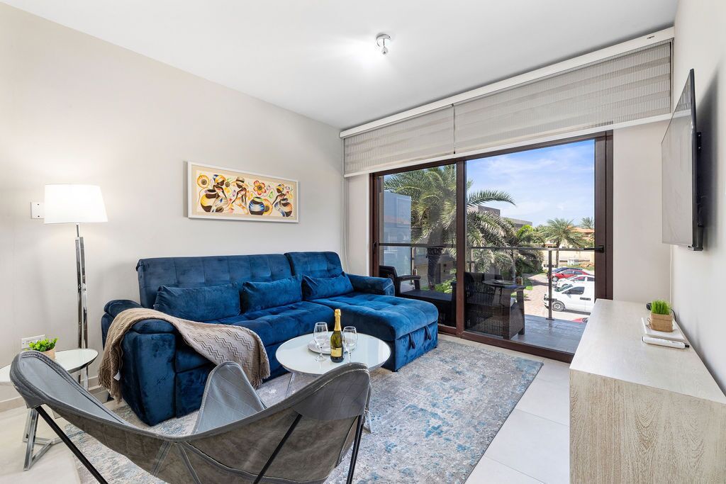 Modern living room with plush blue sofa, stylish decor, large windows, and balcony views.