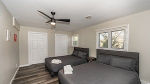 Une chambre avec deux lits, un ventilateur de plafond, une fenêtre avec des stores et une porte.