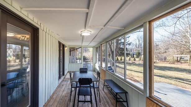 Un patio couvert avec une terrasse en bois, une table et des chaises, et de grandes fenêtres donnant sur l’extérieur.